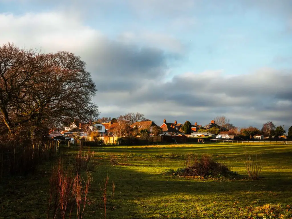 A green field with a cluster of houses on the other side on the approach to Lymington.