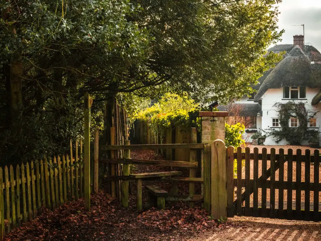 A gate leading to a trail down the side of the white house with a thatched roof.