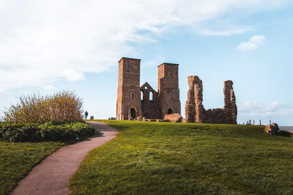 The Reculver Towers on a grassy patch with a winding trail on the left on the walk from Herne Bay to Margate.