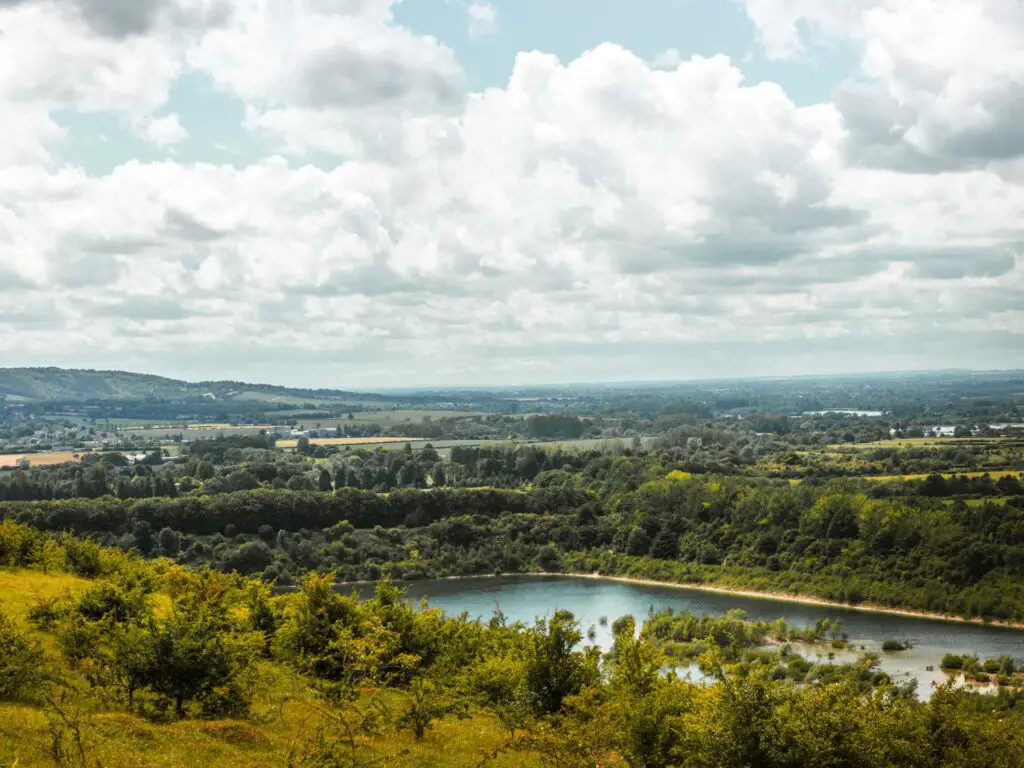 A lake down in the valley in the Chilterns. It is surrounded by lots of green of the trees, pushes and fields.