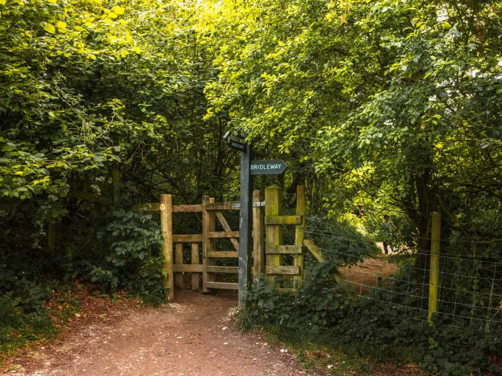 The trail as it goes though a gate and into the woodland. There is signage at the gate.