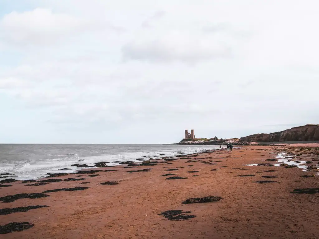 A sandy beach leading to the sea and the Reculver towers up ahead.