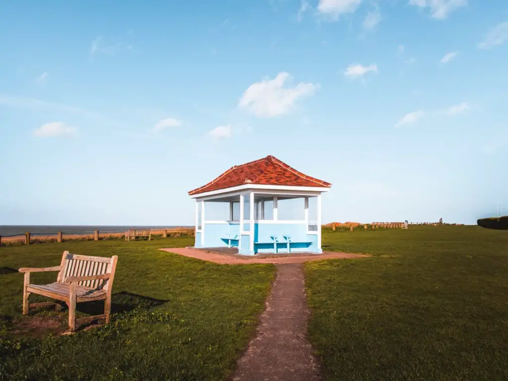 A large grass patch with a path leading to a blue bench hut with a red roof.
