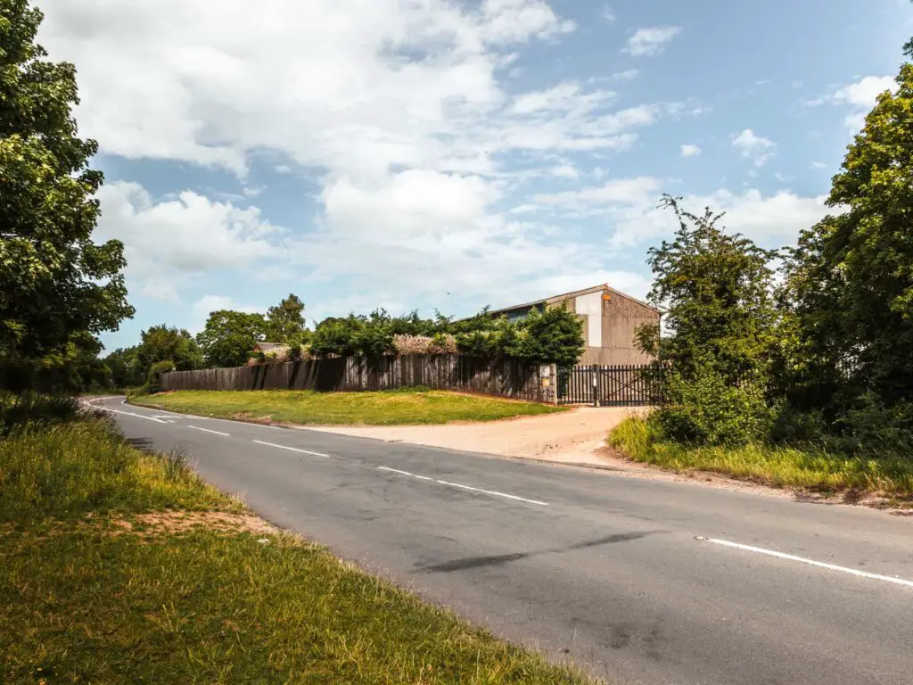 A main road with grassy banks on either side. The sky is blue with a few white clouds.