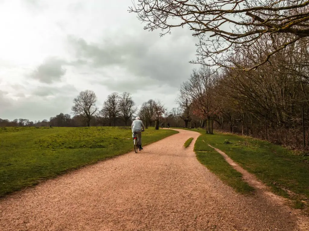 A man cycling on the Tamsin trail in Richmond Park. It is a cloudy day.