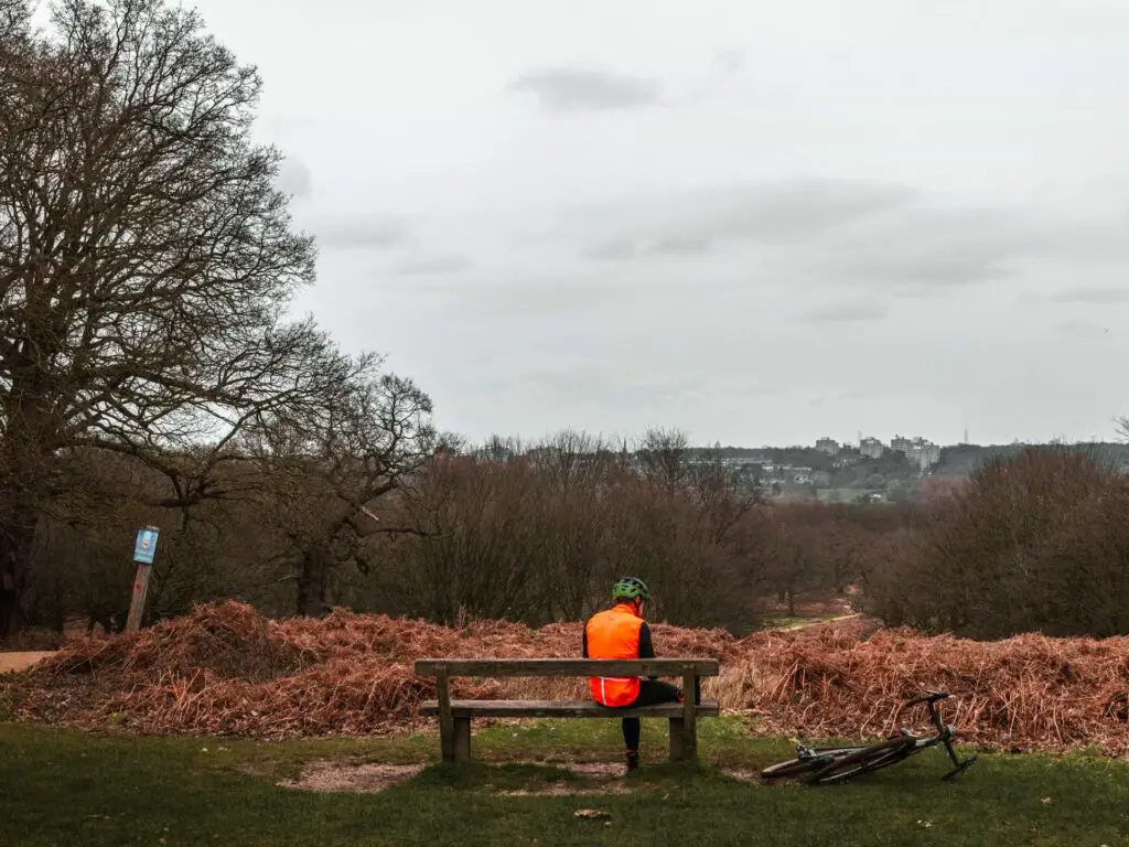 A man sitting on a bench on a hill in Richmond Park. His bike is laying by his side.