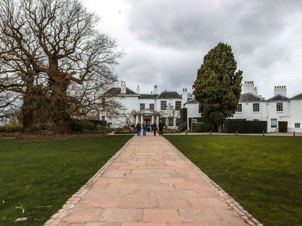 Pembroke Lodge in Richmond Park. There is a path leading to it with people walking on the path. 