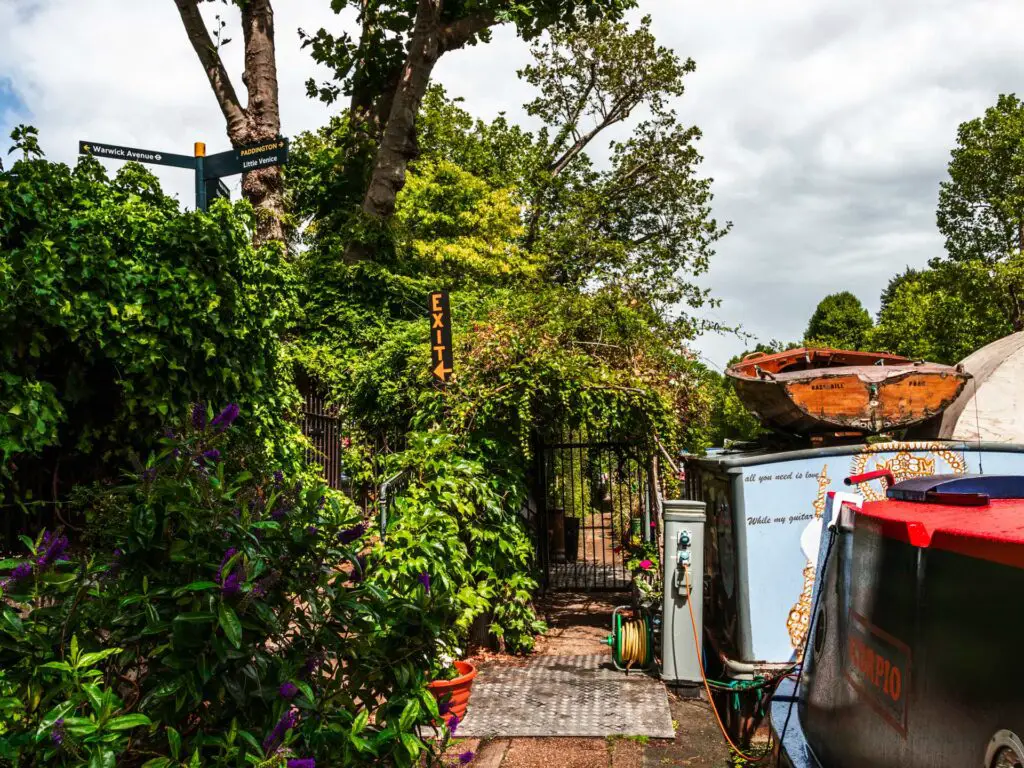 The path lined with bushes on the left and canal boats on the right. 