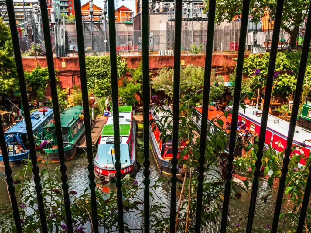 Looking through the black fence railings at the colourful canal boats below on the Regents Canal.