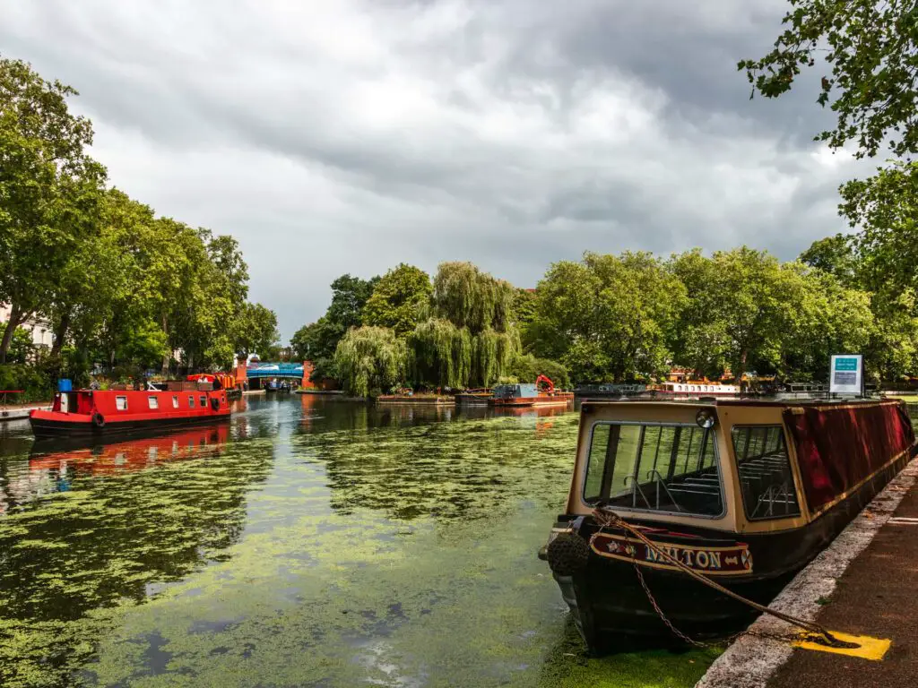 The start of the walk in Little Venice, with a few canal boats on the water and lots of green trees surrounding the canal.