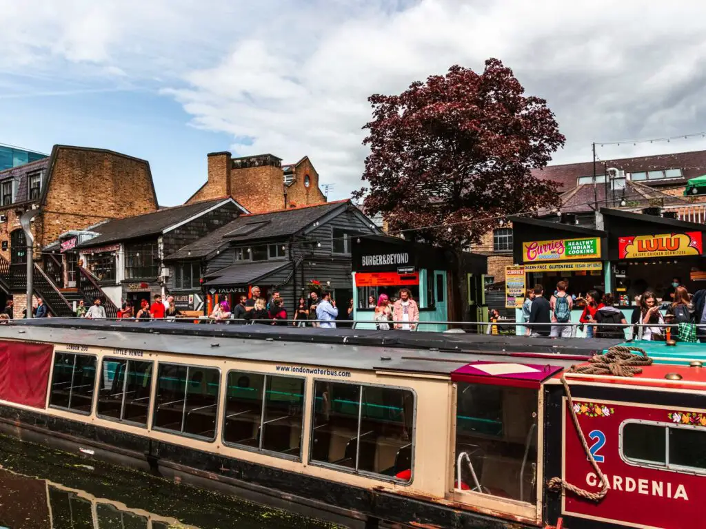 Camden food stalls with lots of people and a barge ion the foreground. 