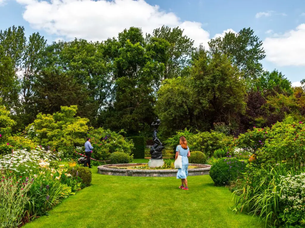 The green lawn of St Johns Lodge surrounded by greenery. There is a women and a man walking on the lawn.