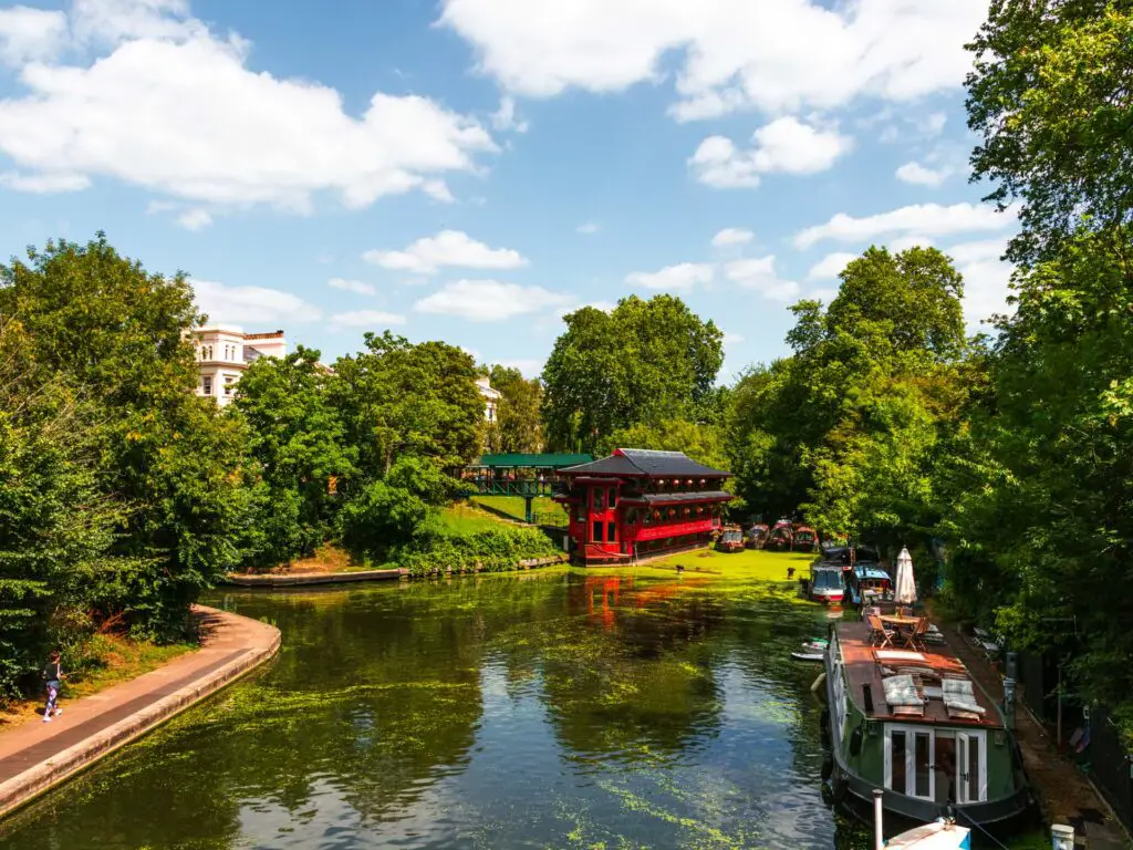 Regents canal surrounded by trees on the walk from Regents Park to Primrose Hill. There is a canal boat in the canal.