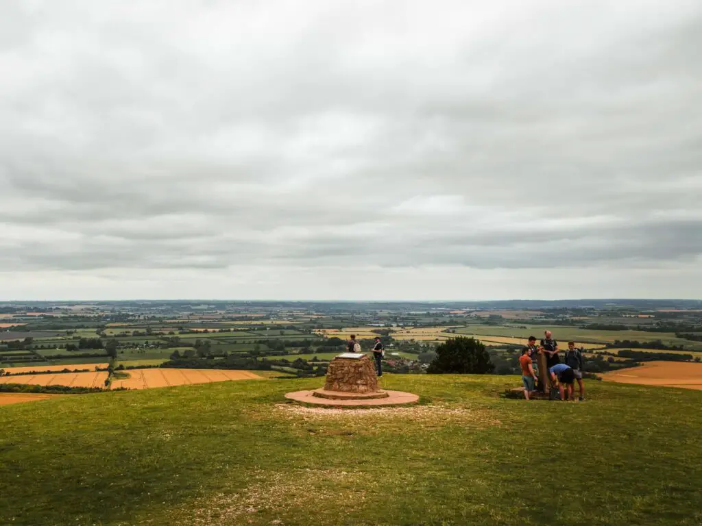 The top of Ivinghoe Beacon on the circular walk from Tring. There are a few people walking along the top with views of fields as far as the eye can see.