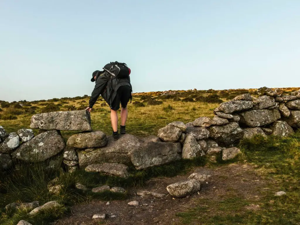 A man (Oliver) climbing over a stone wall in Dartmoor National Park.