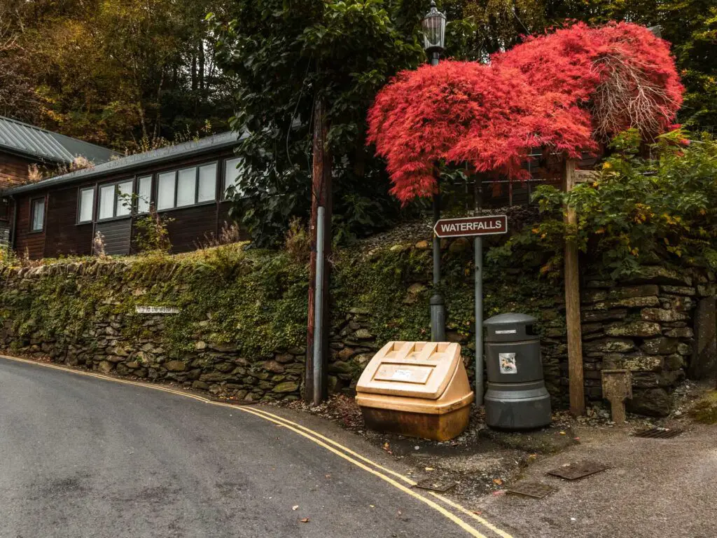 The waterfall sign next to the brick wall and road in Ambleside.