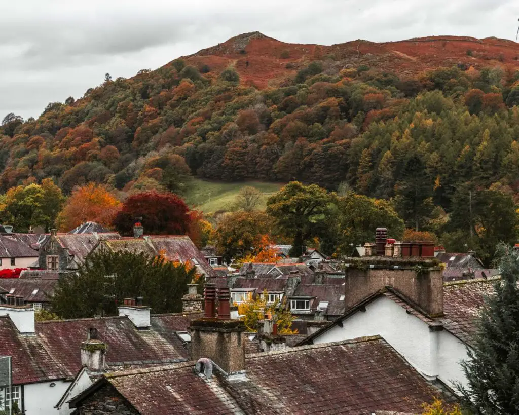 A view of rooftops of Ambleside with a big hill as a backdrop, with lots of Autumn coloured trees on it.