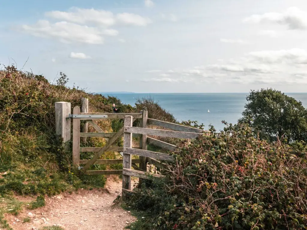 A wooden gate surrounded by brushes and shrubbery on the walk from Swanage to old Harry Rocks. The blue sea is visible in the background.