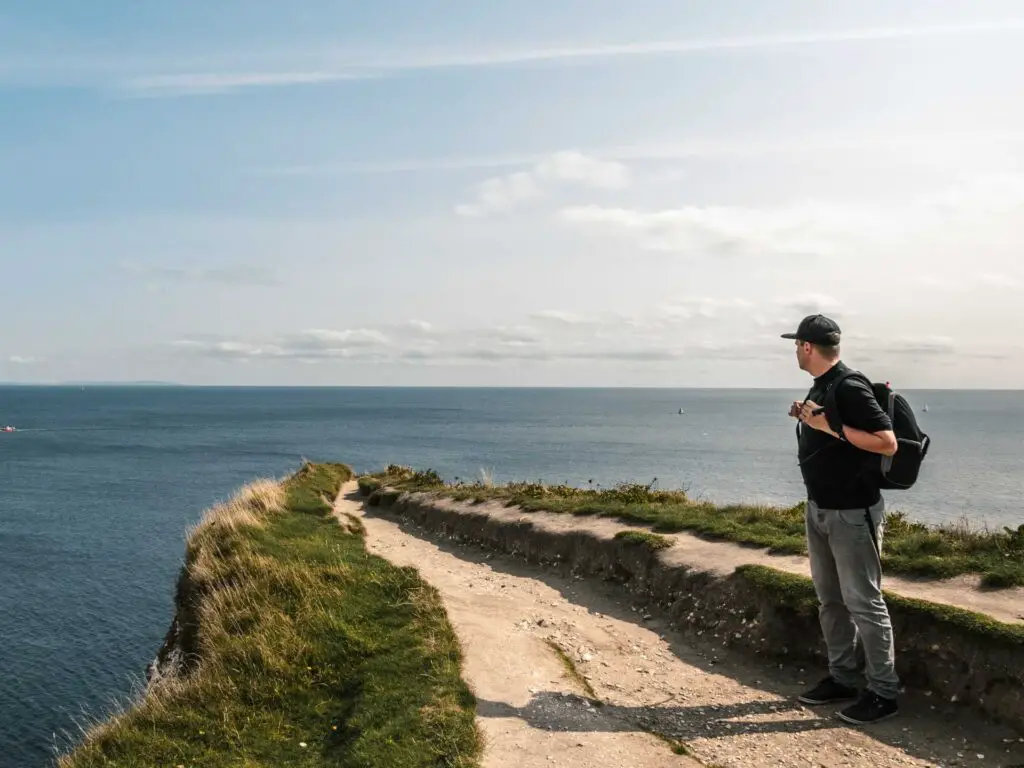 A man standing at Old Harry Rocks looking out to the dark blue sea in the distance. 