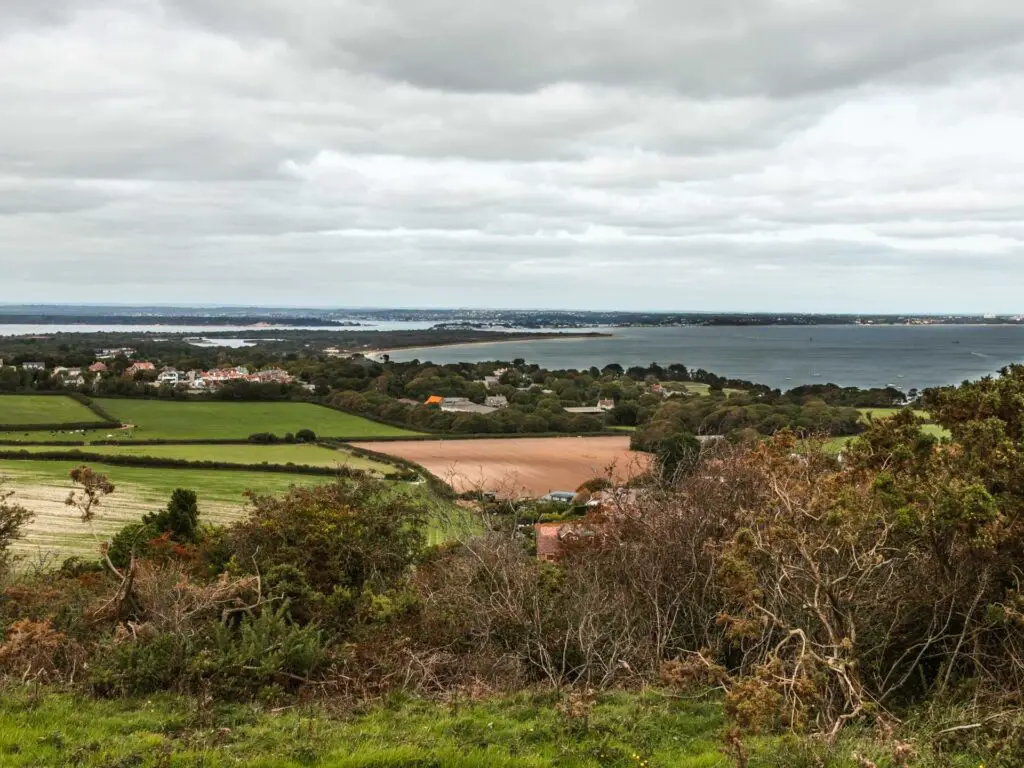 Views downhill to the green and orange fields with the blue sea in the distance.