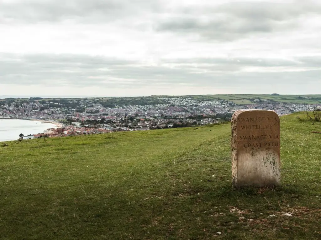 A stone signage marking Swanage and the coast past towards the end of the walk from Old Harry rocks. The town of Swanage is visible in the distance. 