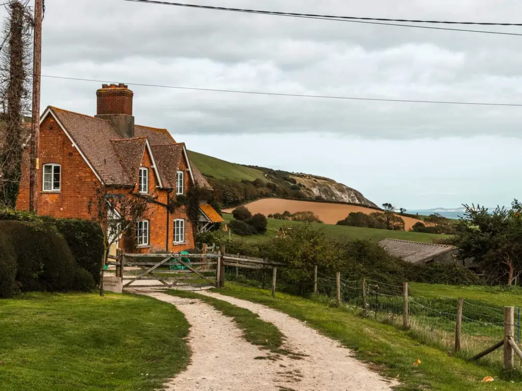 A red brick house with the green cliffside in the distance behind it. on the walk back to Swanage from Old Harry Rocks.