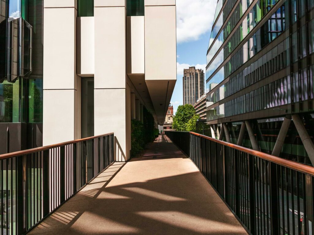 A bridge path with black metal railings on either side, leading along to buildings in the city.