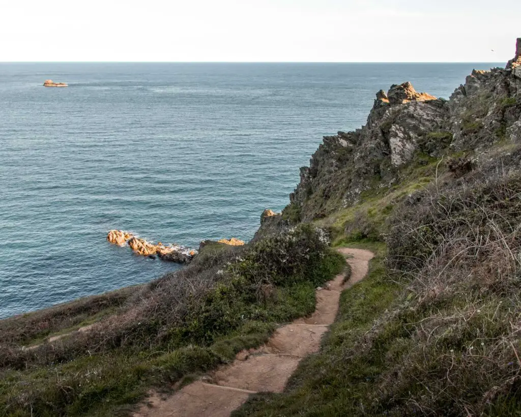 Steps on the side of the green grass hill leading to the blue sea.