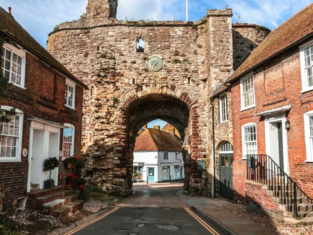 The brick arch of Landgate in Rye with the road running through it and brick houses neck to it. There is a clock above the arch.