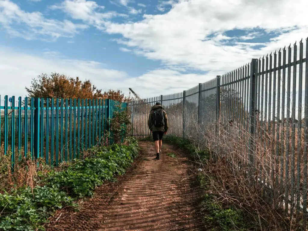 Oliver walking on the wide dirt trail with metal railing fences on either side.