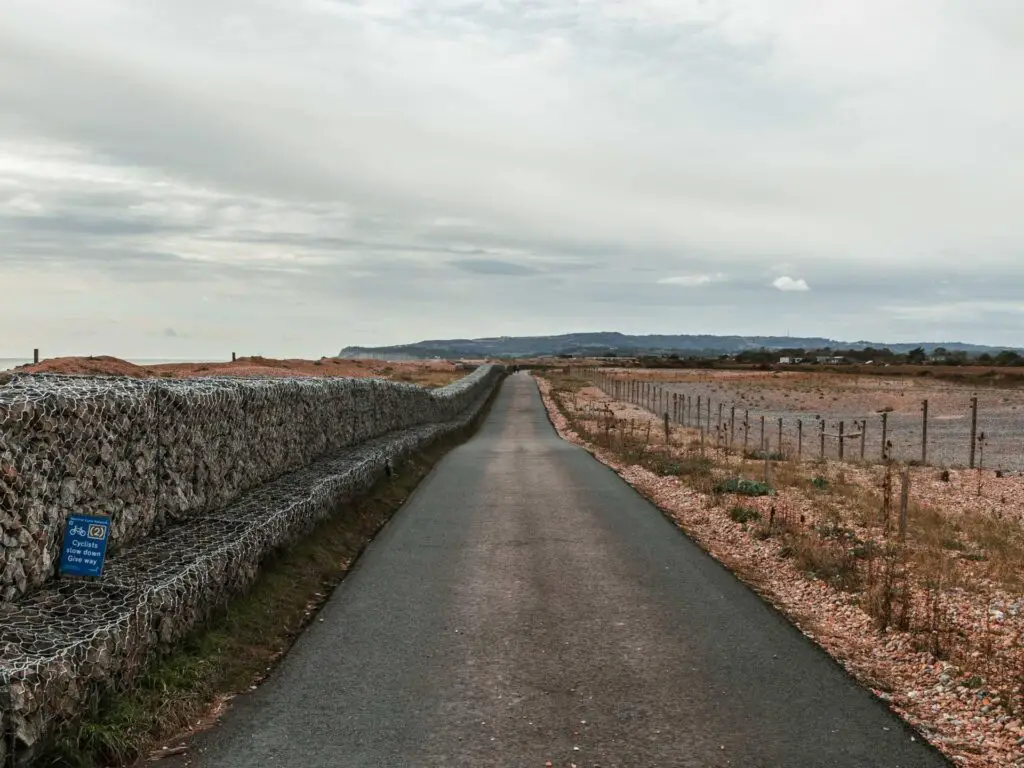 A long walking path with a stone wall on the left and shingle to the right.