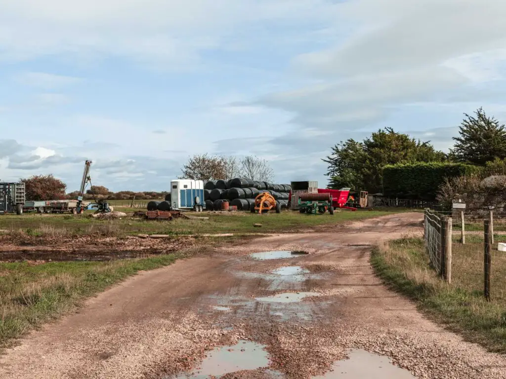 A trail with some puddles. There is farm equipment on the other side on the grass.