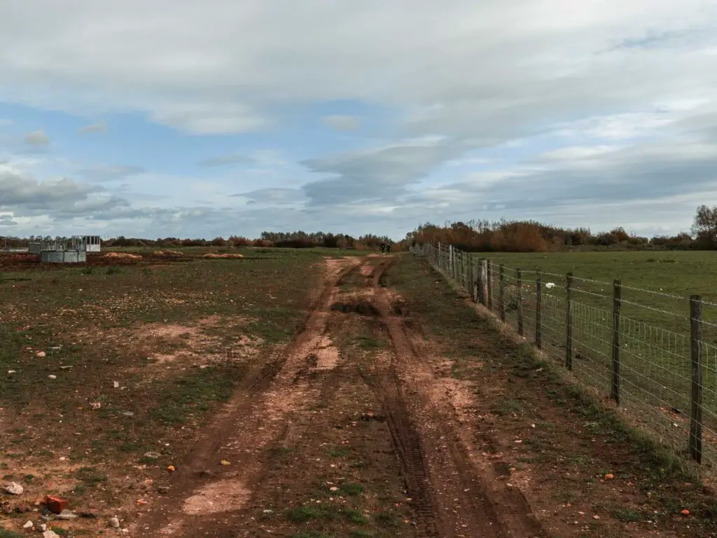 Dirt tracks leading through a field with a metal fence on the right.