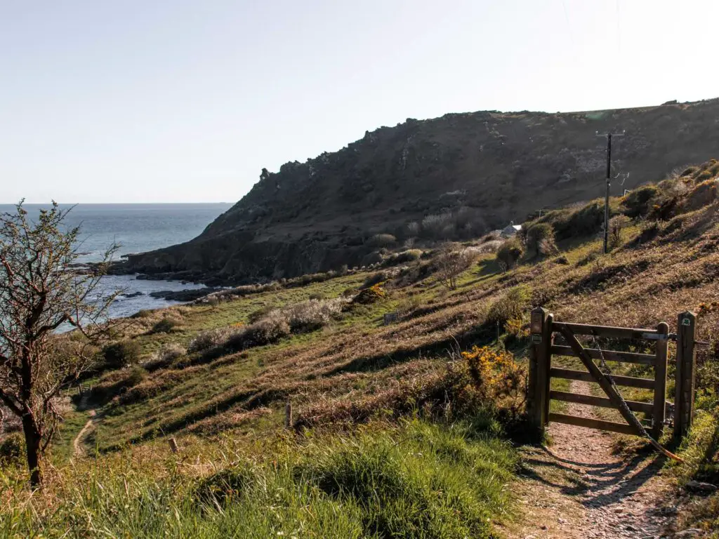 The dirt trail leading through a wooden gate with the cliffs in the background.