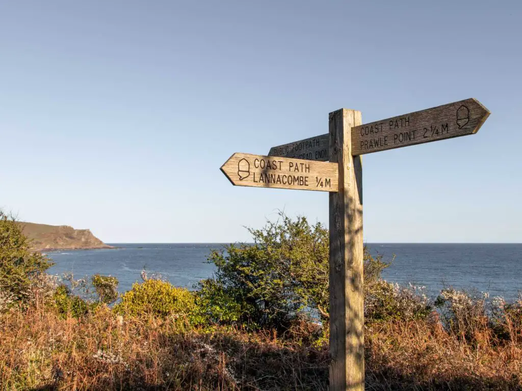 Wooden coast path signage pointing g in three directions. The blue sea is in the background.