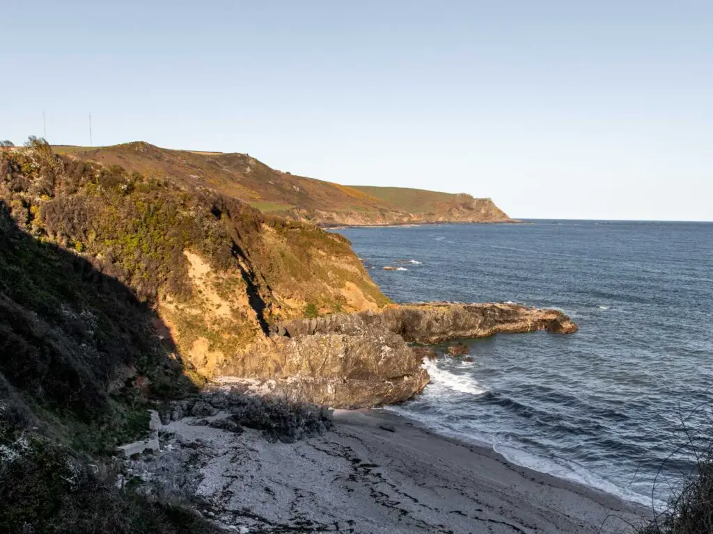 A sandy beach shaded behind the cliffs in south Devon. The sea is blue.