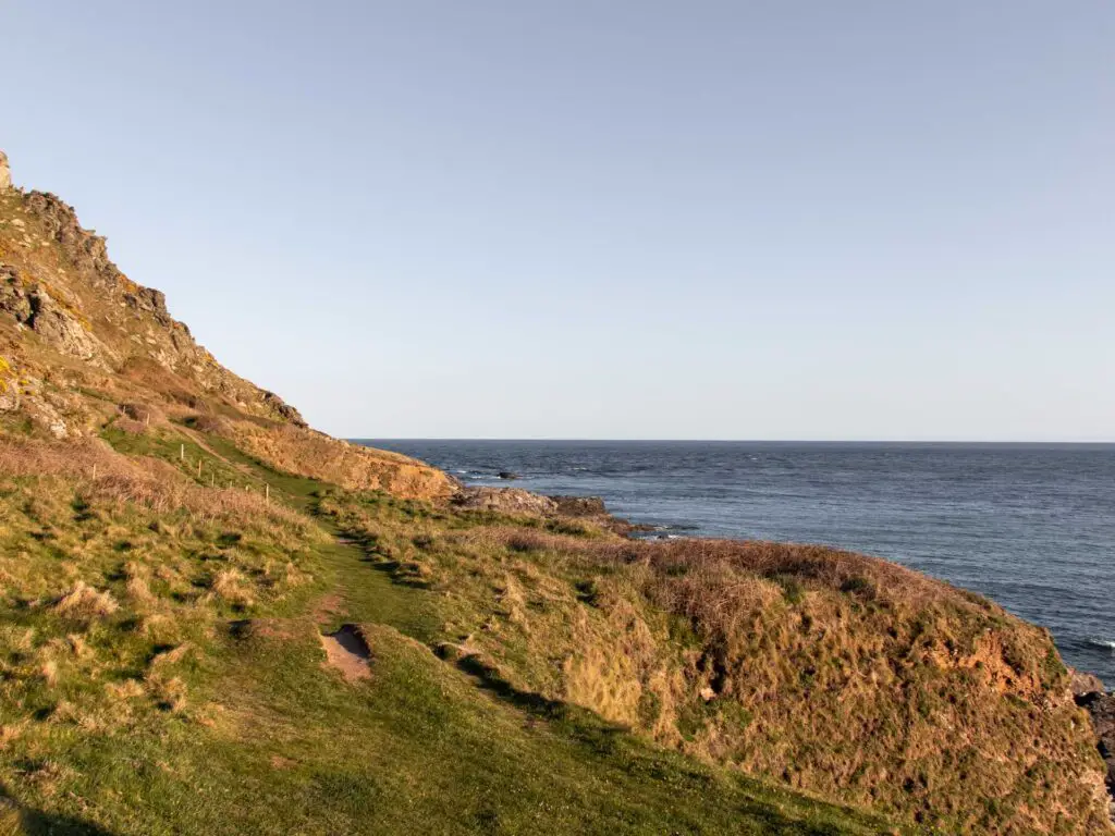 The green grass trail running along the side of a hill with the blue sea to the right.