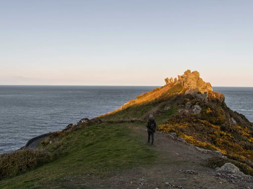 A man walking along the ridge with jagged rocks ahead and the blue sea on the background.