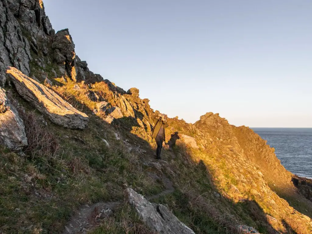 A man standing on the side of the rocky hill on the walk to start point lighthouse. 