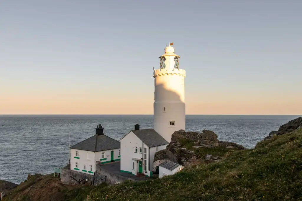 White buildings and a lighthouse on the edge of the rocky peninsula on the start point lighthouse walk. The blue is there backdrop.