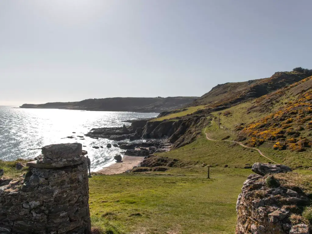 A view ahead of the cliffy coastline on the start point lighthouse walk. There is a sandy beach visible at the bottom of the cliffs. There is a narrow dirt trail running along the top of the cliffs.