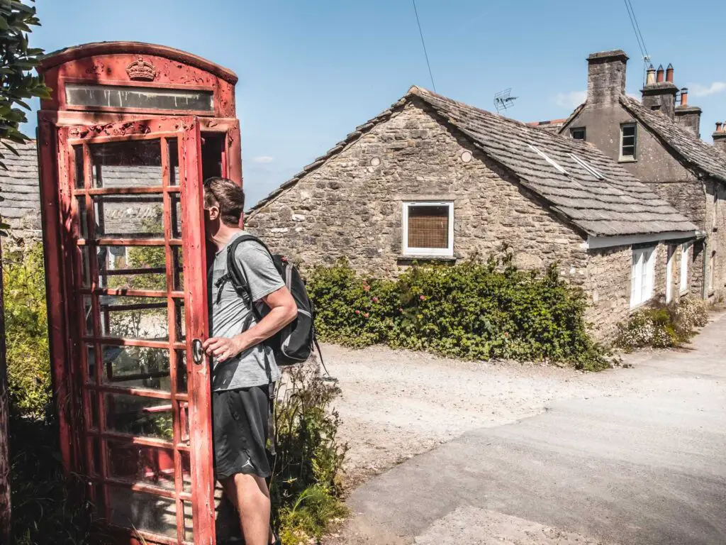 A man looking in a red telephone box with stone and flint houses behind, in Kingston, Dorset.