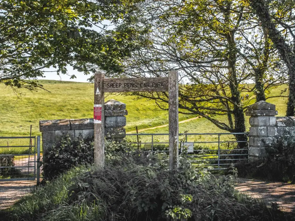 A wooden signpost saying sheep pen car park. There is a gate behind it leading to a grass field.