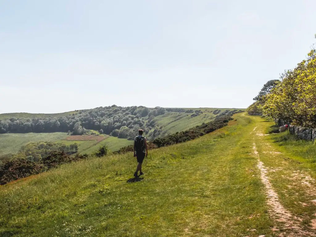 A man walking along a grass ridge with the valley just visible to the left.