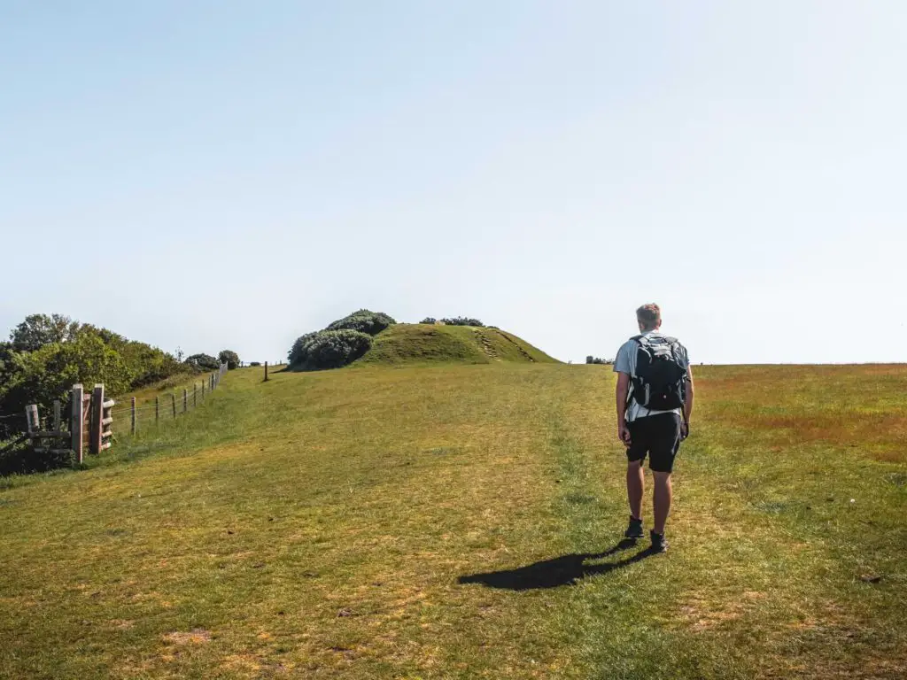 A man walking across a grass field to a small hill ahead.