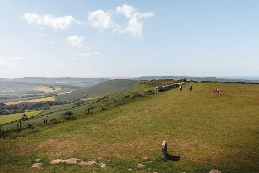 A field with hills in the diatcue and a few people walking in the field.