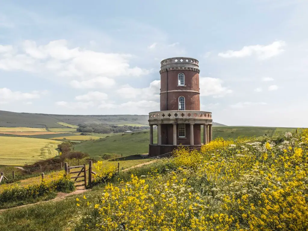 Clavell Tower behind the yellow flowers. There are hills and fields behind the town. 