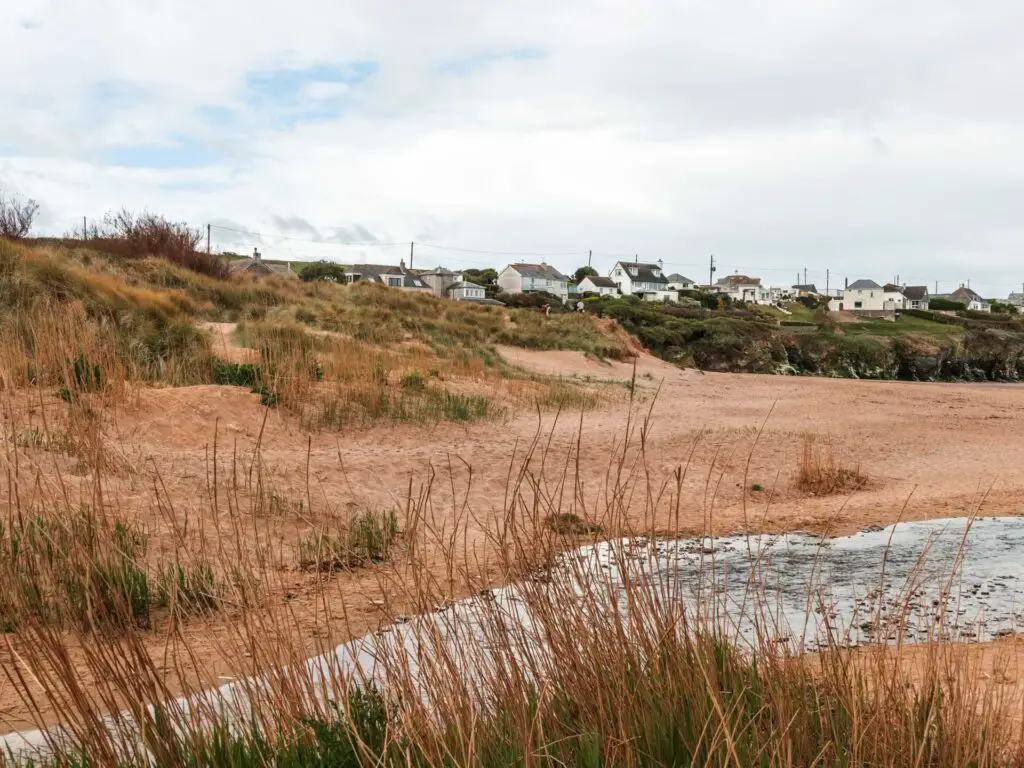 Porthocthan beach with a stream of water running through it and some houses on the hilltop on the other side of the beach.