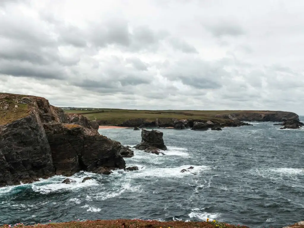 The rugged dark colours cliff coastline with rocks justing out of the sea on the coastal walk from Porthcothan to Treyarnon in Cornwall.