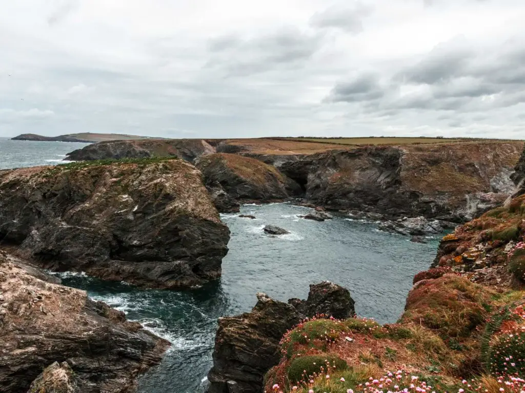 The sea in Cornwall, surrounded by craggy cliffs and rocks on the walk along the South West Coast Path.